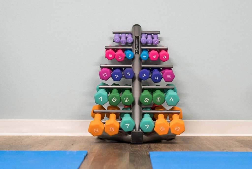 Colorful vinyl dumbbells stacked in a rack with blue yoga mats visible on floor nearby